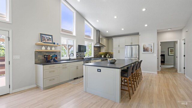 kitchen featuring wall chimney exhaust hood, stainless steel appliances, dark countertops, a sink, and backsplash