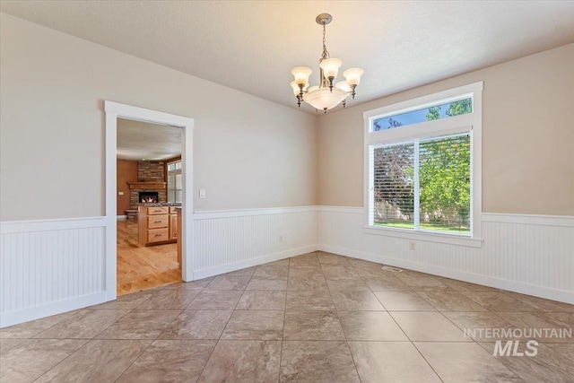 1112 W Belknap Dr, Nampa, ID 83686 - unfurnished room featuring wainscoting, a chandelier, and a stone fireplace