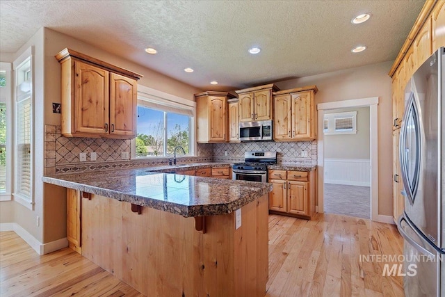 1112 W Belknap Dr, Nampa, ID 83686 - kitchen with appliances with stainless steel finishes, a peninsula, a textured ceiling, light wood-style floors, and a kitchen bar