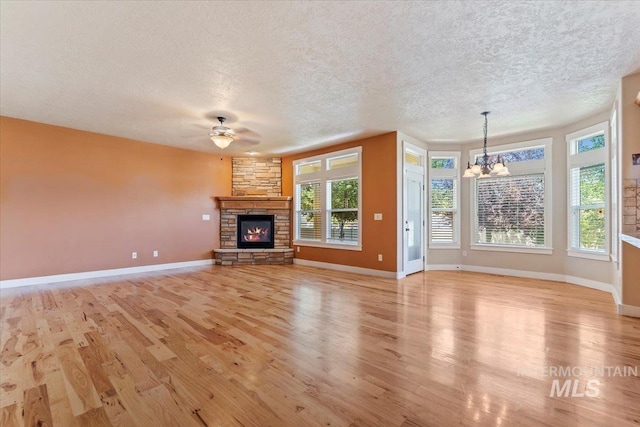 1112 W Belknap Dr, Nampa, ID 83686 - unfurnished living room featuring a chandelier, light wood-style flooring, a textured ceiling, ceiling fan, and a stone fireplace