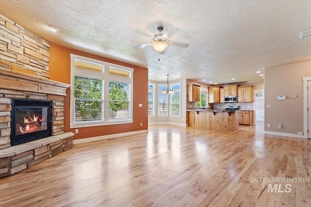 1112 W Belknap Dr, Nampa, ID 83686 - unfurnished living room with a textured ceiling, a stone fireplace, light wood finished floors, a ceiling fan, and a chandelier