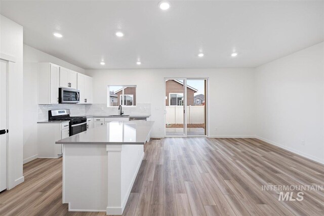 kitchen featuring stainless steel appliances, a kitchen island, white cabinetry, decorative backsplash, and light hardwood / wood-style flooring