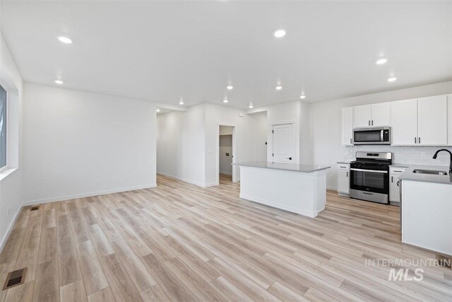 kitchen with appliances with stainless steel finishes, sink, light hardwood / wood-style floors, and a center island