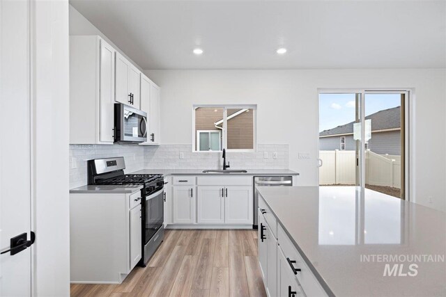 kitchen with stainless steel appliances, white cabinets, sink, tasteful backsplash, and light hardwood / wood-style flooring