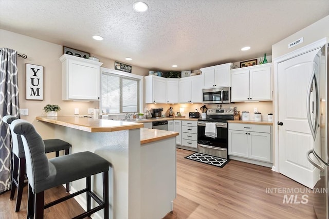 kitchen featuring appliances with stainless steel finishes, kitchen peninsula, a breakfast bar area, and white cabinets