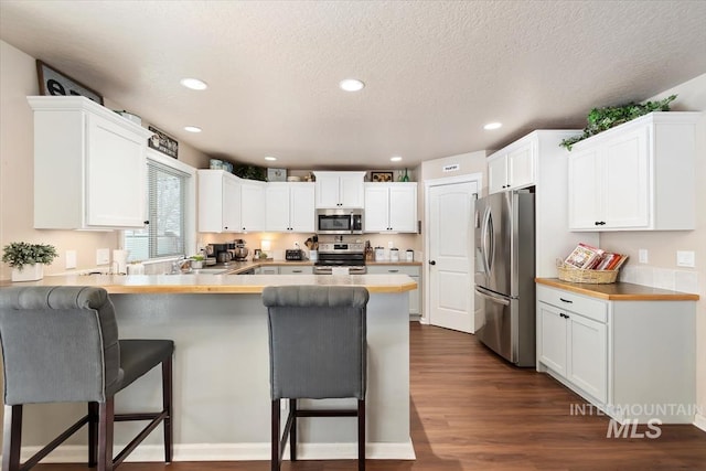 kitchen with appliances with stainless steel finishes, a kitchen breakfast bar, kitchen peninsula, and white cabinets