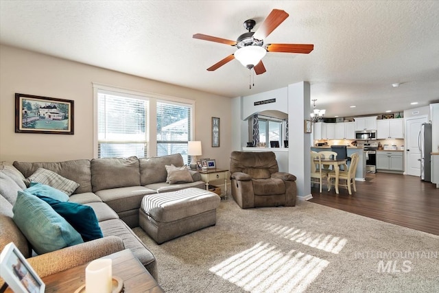 living room featuring dark wood-type flooring, ceiling fan with notable chandelier, and a textured ceiling