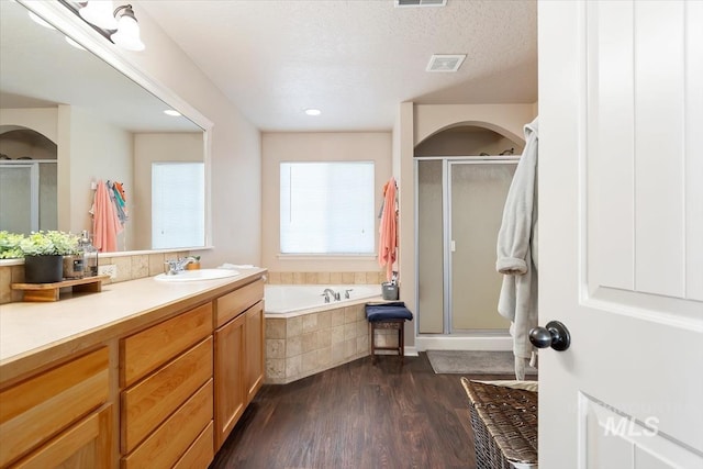 bathroom featuring wood-type flooring, separate shower and tub, vanity, and a textured ceiling