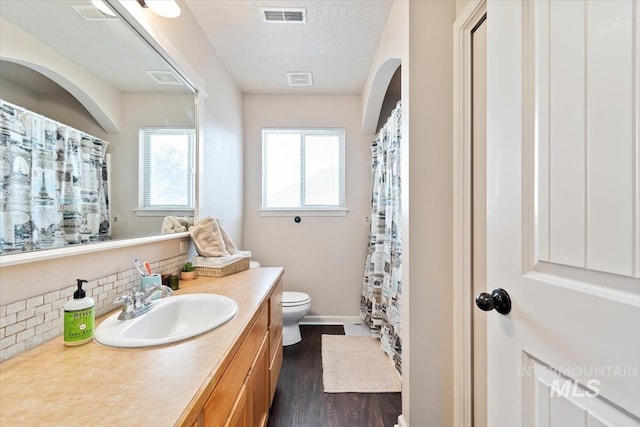 bathroom with toilet, wood-type flooring, a textured ceiling, vanity, and backsplash