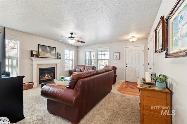 carpeted living room featuring ceiling fan, a fireplace, and a textured ceiling