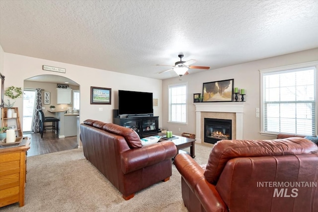 living room with a textured ceiling, carpet floors, a tile fireplace, and ceiling fan