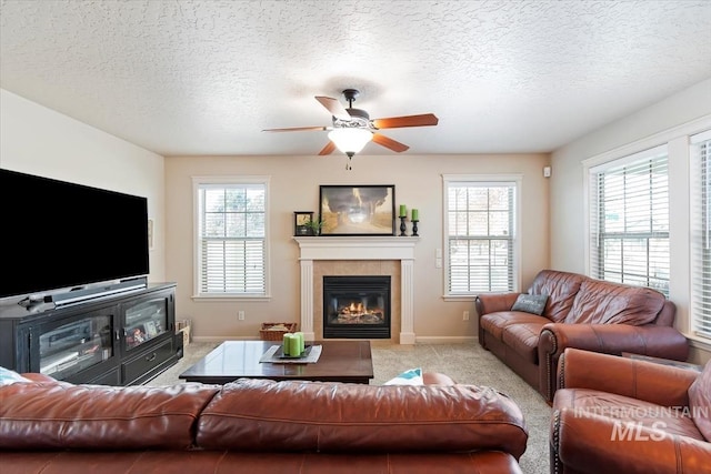 living room with a tile fireplace, light carpet, ceiling fan, and a textured ceiling