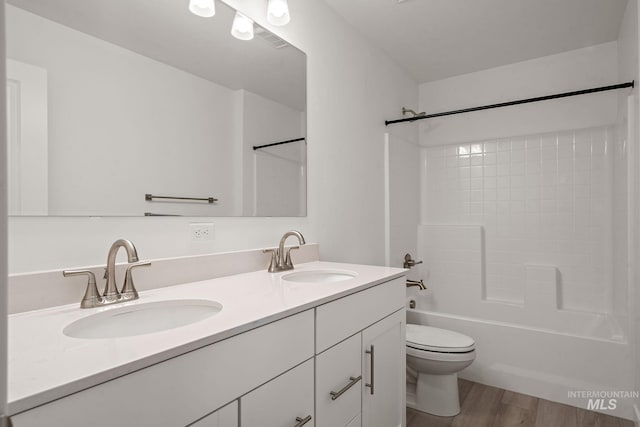 bathroom with double vanity, toilet, wood finished floors, and a sink