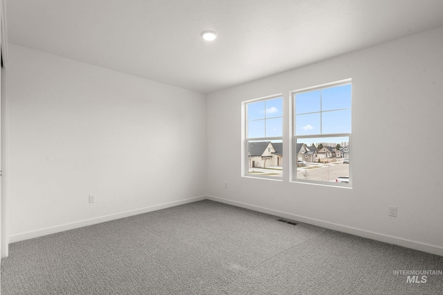 unfurnished room with carpet, visible vents, and baseboards