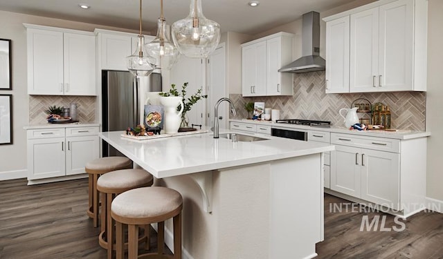 kitchen featuring a sink, white cabinets, wall chimney range hood, dark wood-style floors, and an island with sink