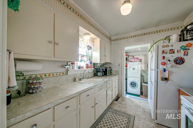 kitchen with white cabinets, white refrigerator, stacked washing maching and dryer, and sink