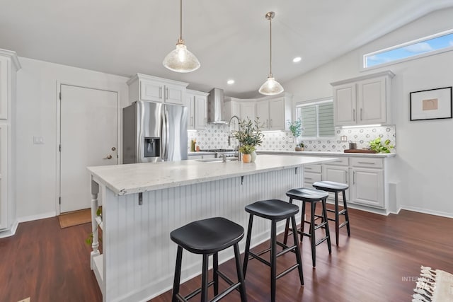 kitchen with white cabinetry, stainless steel fridge with ice dispenser, wall chimney exhaust hood, and a kitchen island with sink