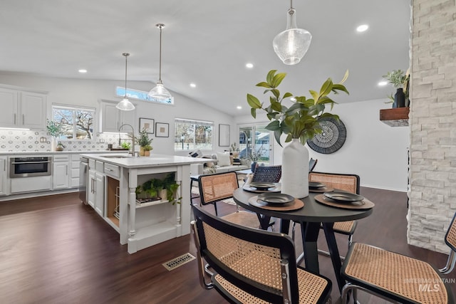 kitchen featuring stainless steel oven, dark hardwood / wood-style flooring, an island with sink, and hanging light fixtures