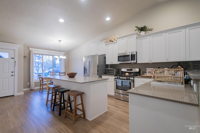 kitchen featuring a center island, decorative backsplash, decorative light fixtures, white cabinetry, and stainless steel appliances