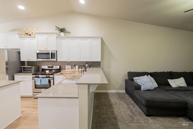 kitchen featuring kitchen peninsula, tasteful backsplash, stainless steel appliances, vaulted ceiling, and white cabinetry