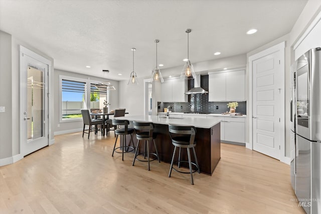 kitchen featuring wall chimney range hood, smart refrigerator, a breakfast bar area, light countertops, and tasteful backsplash