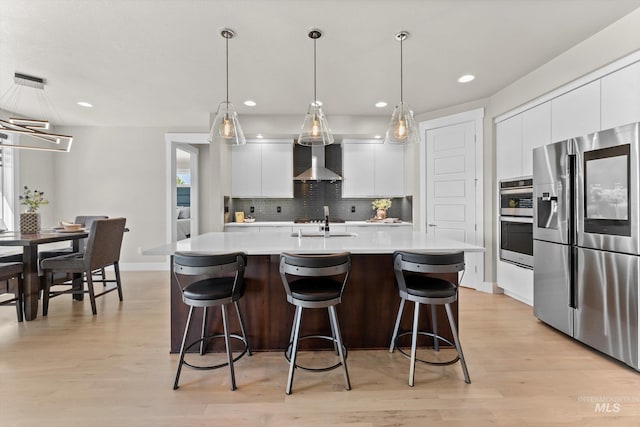kitchen with stainless steel appliances, wall chimney exhaust hood, modern cabinets, light wood-style floors, and recessed lighting
