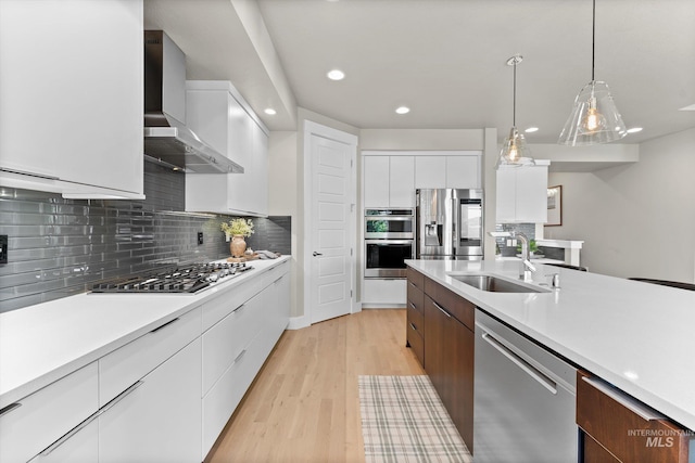 kitchen featuring stainless steel appliances, a sink, modern cabinets, wall chimney range hood, and white cabinets