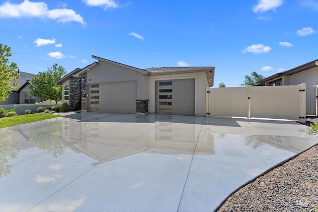 view of front of home with a gate, fence, an attached garage, concrete driveway, and stone siding