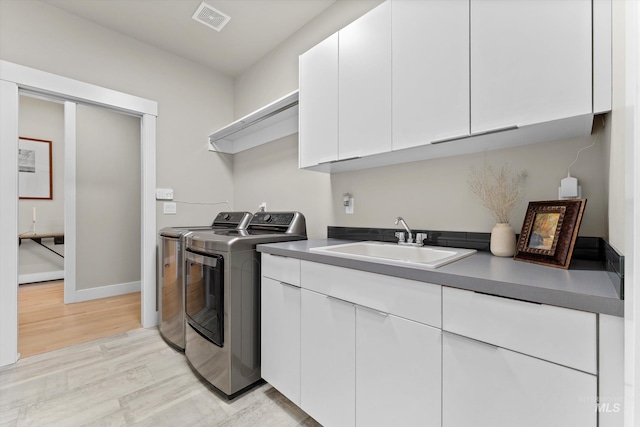 clothes washing area with independent washer and dryer, light wood-style flooring, cabinet space, and baseboards