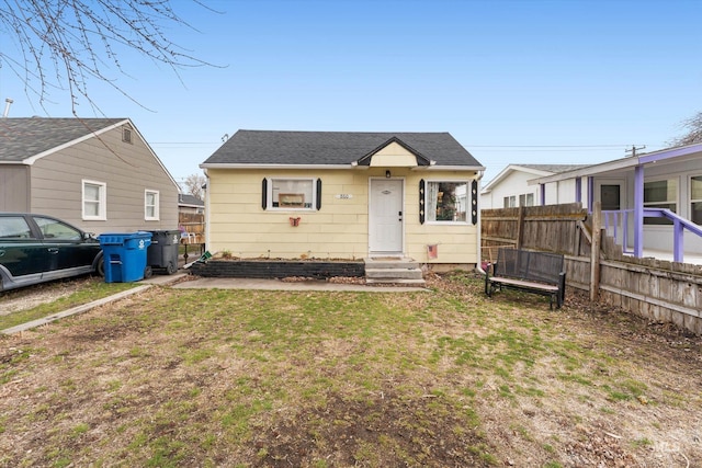 bungalow-style home featuring entry steps, roof with shingles, fence, and a front lawn