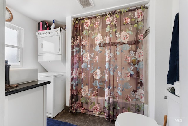 clothes washing area featuring laundry area, dark tile patterned floors, stacked washing maching and dryer, and visible vents