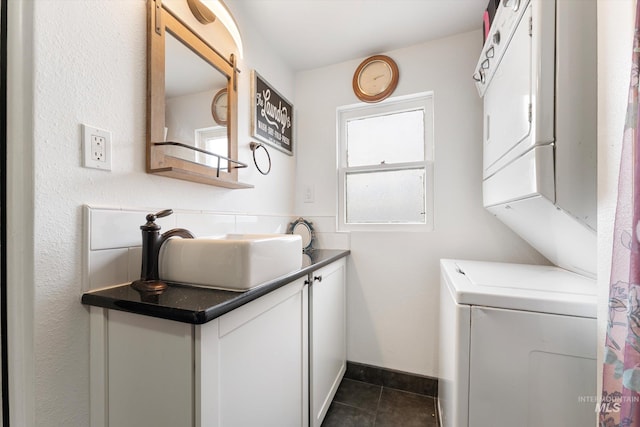 laundry room with a sink, baseboards, stacked washer / dryer, and dark tile patterned flooring