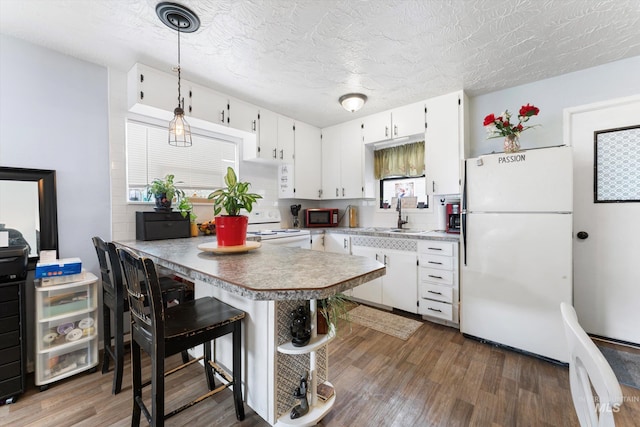 kitchen featuring white appliances, white cabinetry, a sink, and wood finished floors