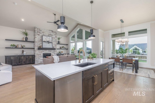 kitchen featuring a sink, a stone fireplace, light wood-style flooring, stainless steel microwave, and light countertops