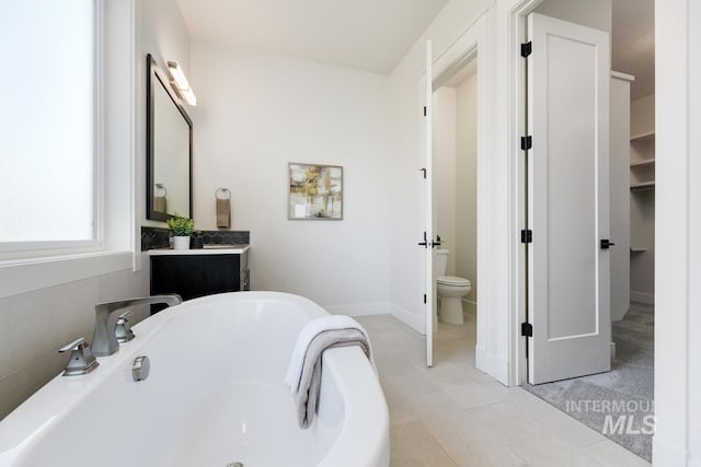 bathroom with a freestanding tub, toilet, vanity, and baseboards