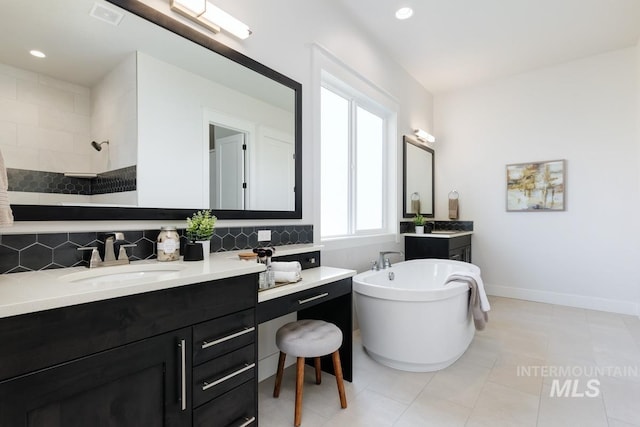 full bath featuring decorative backsplash, walk in shower, a soaking tub, two vanities, and baseboards