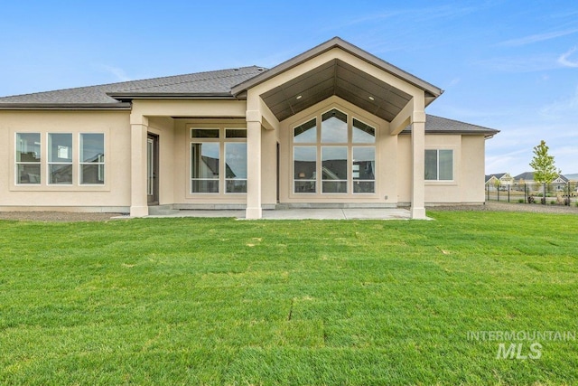back of house featuring a lawn, stucco siding, and a shingled roof