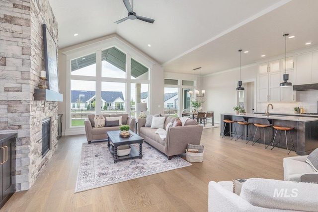 living room featuring ceiling fan, lofted ceiling, a stone fireplace, plenty of natural light, and light wood finished floors