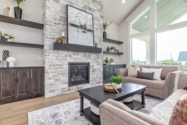 living area featuring light wood-type flooring, a stone fireplace, and vaulted ceiling