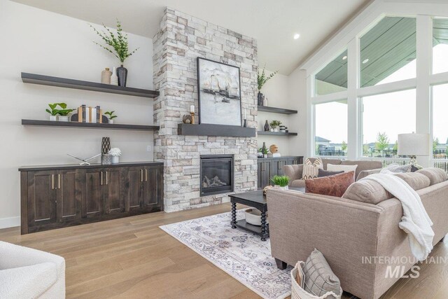 living area with high vaulted ceiling, a stone fireplace, and wood finished floors