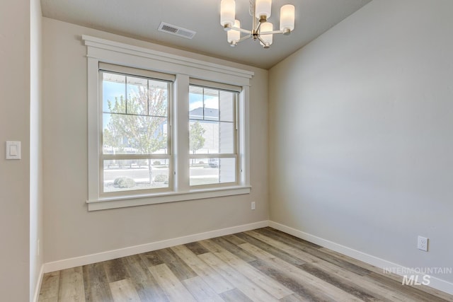 unfurnished room with visible vents, wood finished floors, baseboards, a notable chandelier, and vaulted ceiling
