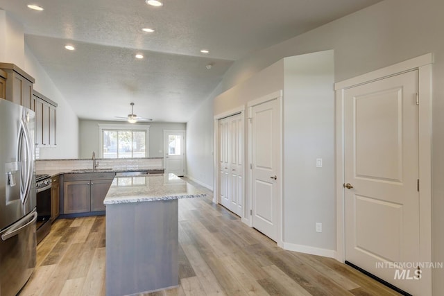 kitchen with a kitchen island, light stone countertops, a sink, appliances with stainless steel finishes, and vaulted ceiling