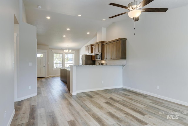 kitchen featuring appliances with stainless steel finishes, vaulted ceiling, light stone counters, ceiling fan with notable chandelier, and recessed lighting