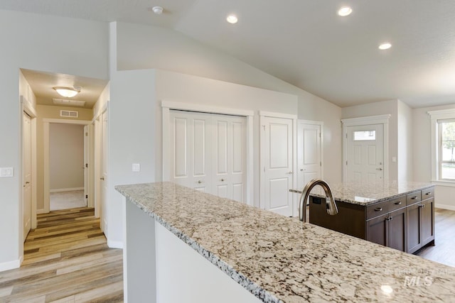 kitchen with dark brown cabinetry, light wood-style floors, baseboards, lofted ceiling, and visible vents