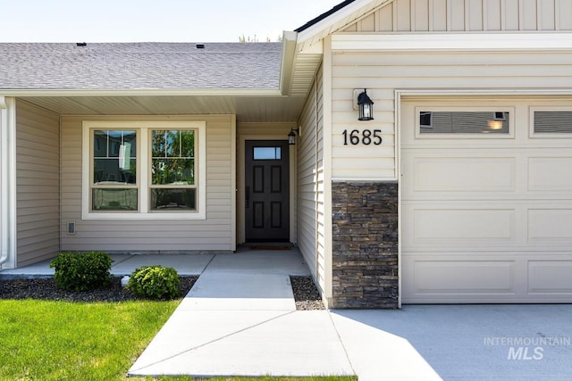 entrance to property featuring a garage, roof with shingles, and stone siding