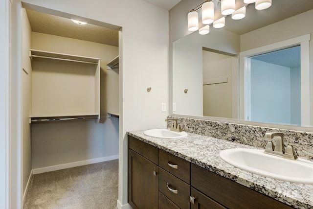 bathroom featuring baseboards, a sink, a walk in closet, and double vanity