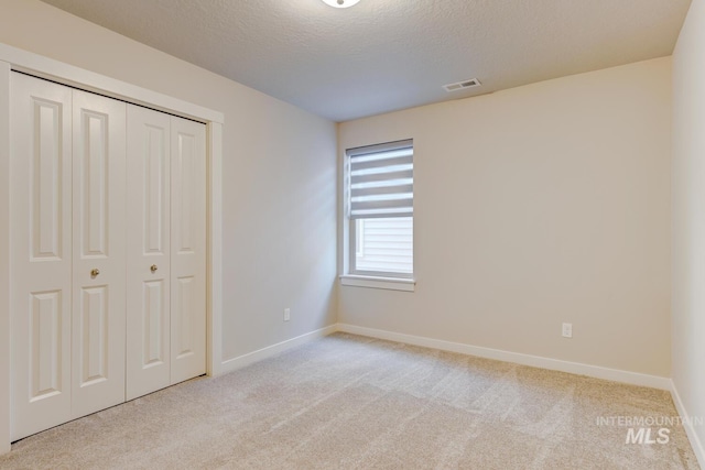 unfurnished bedroom featuring light carpet, a textured ceiling, baseboards, visible vents, and a closet