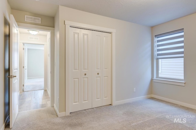 unfurnished bedroom featuring baseboards, light carpet, a closet, and visible vents