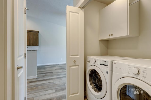 clothes washing area with separate washer and dryer, baseboards, light wood finished floors, and cabinet space