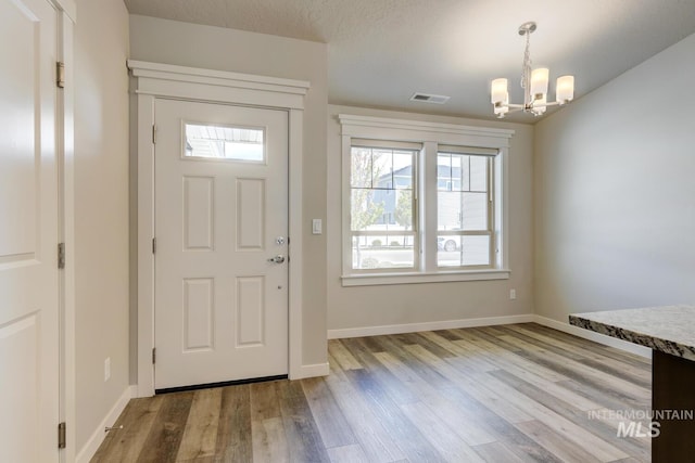 entryway featuring baseboards, a notable chandelier, wood finished floors, and visible vents